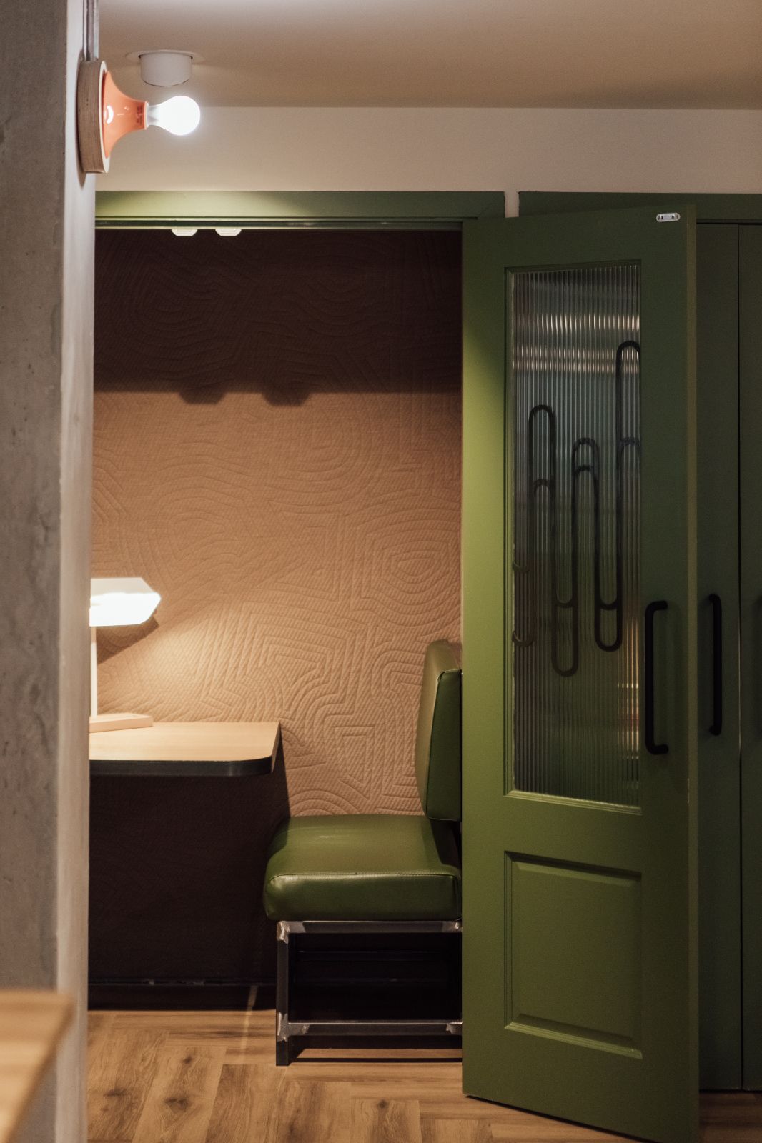 Telephone booth in Hairpin House lobby. Khaki green seat with pale pink fabric coated wall. Green folding doors.